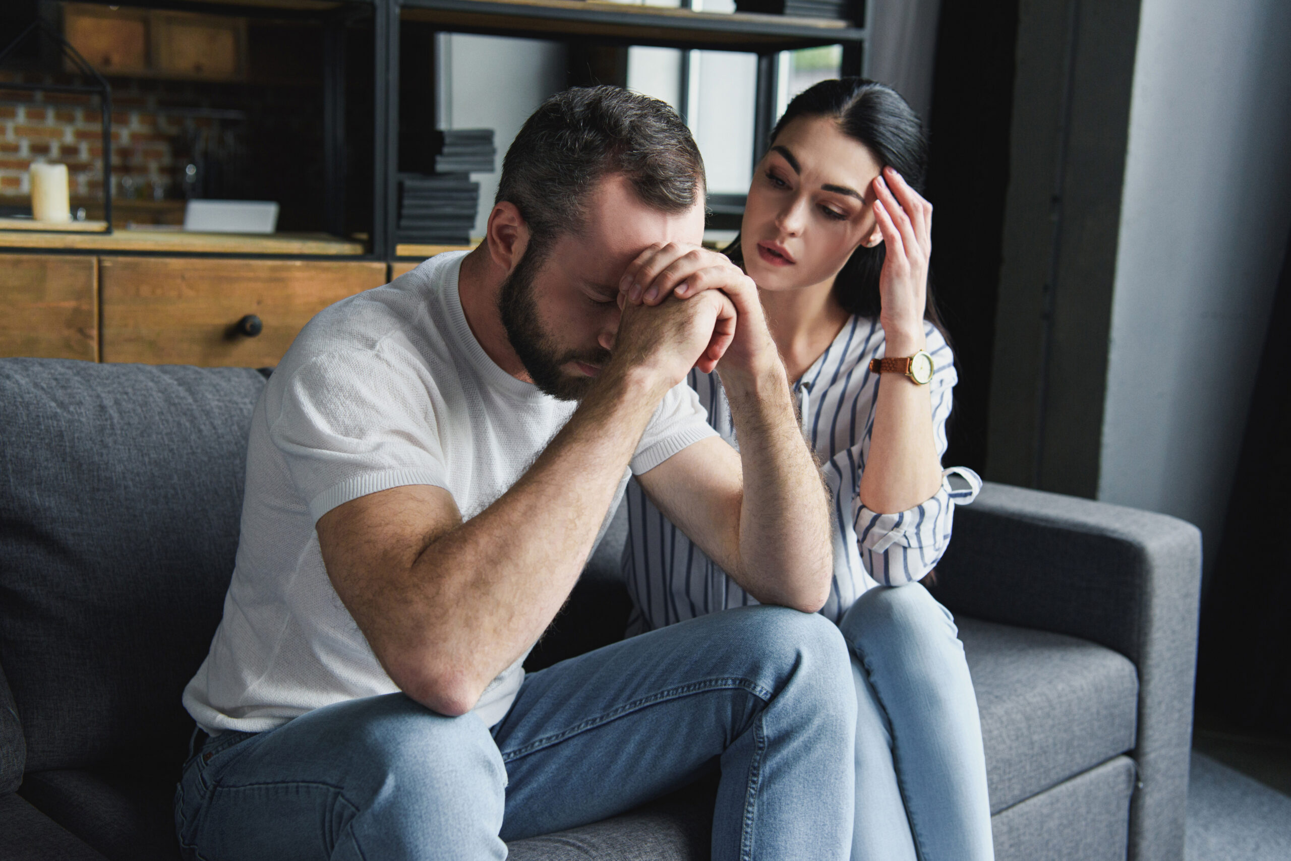 depressed young couple sitting on couch at home after quarrel